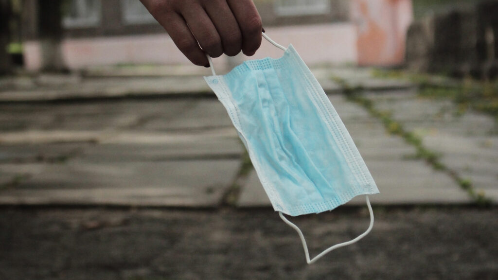 A person holding a disposable mask by the strap.