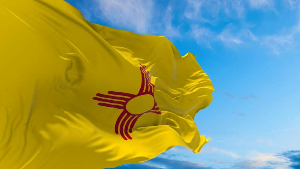 The New Mexico State Flag. Yellow with a red Zia symbol in the middle.