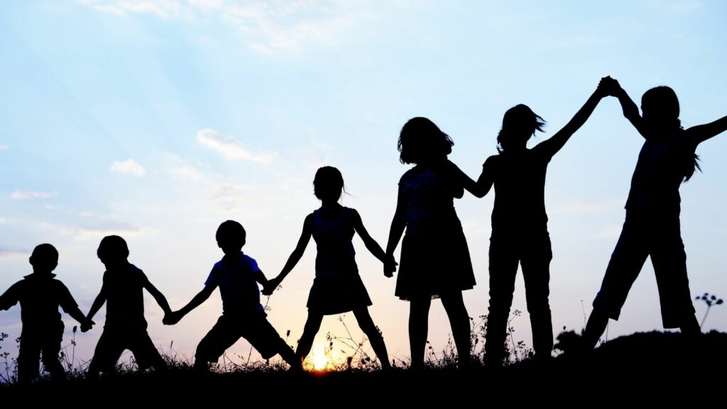 Silhouettes against a blue sky of a chain of children holding hands.