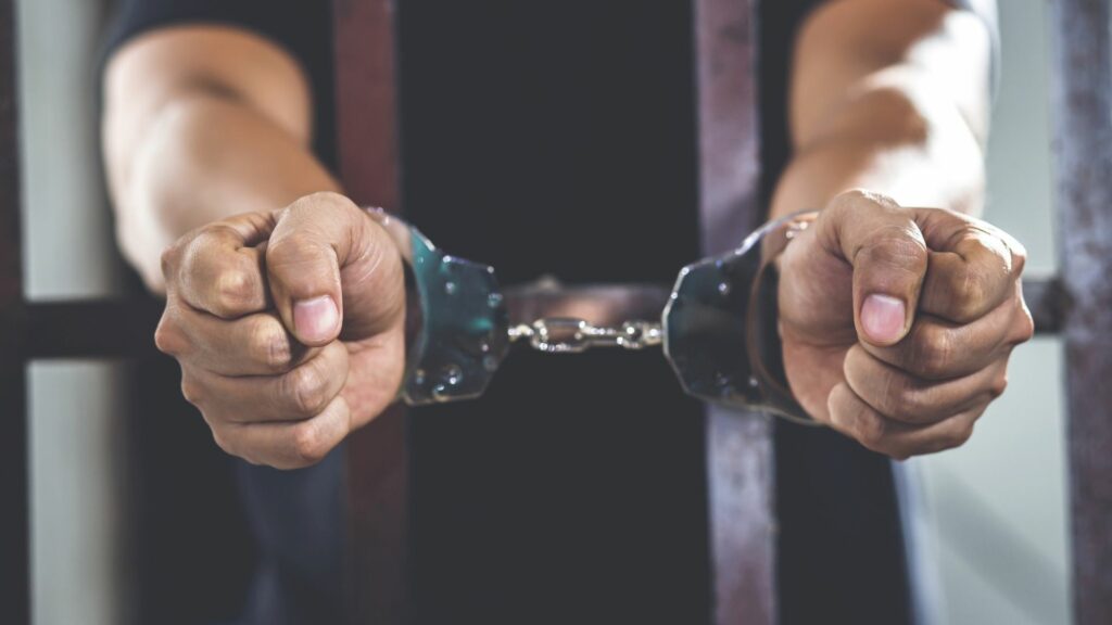 A person in a jail cell wearing hand-cuffs.