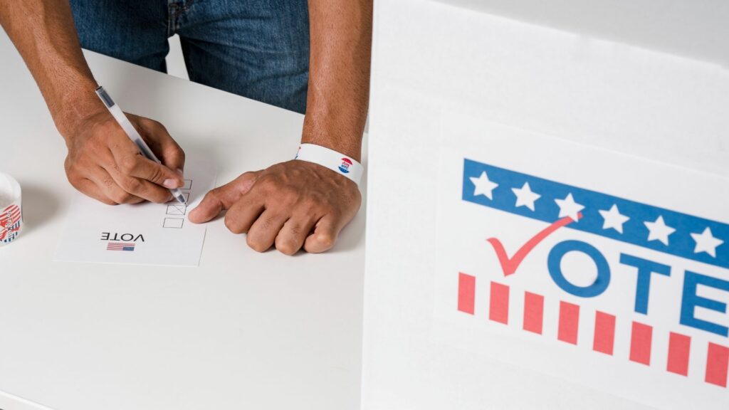 A person writing on a ballot at a voting location.