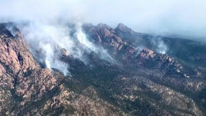 An aerial view of Hermits Peak mountain on fire with lots of smoke.
