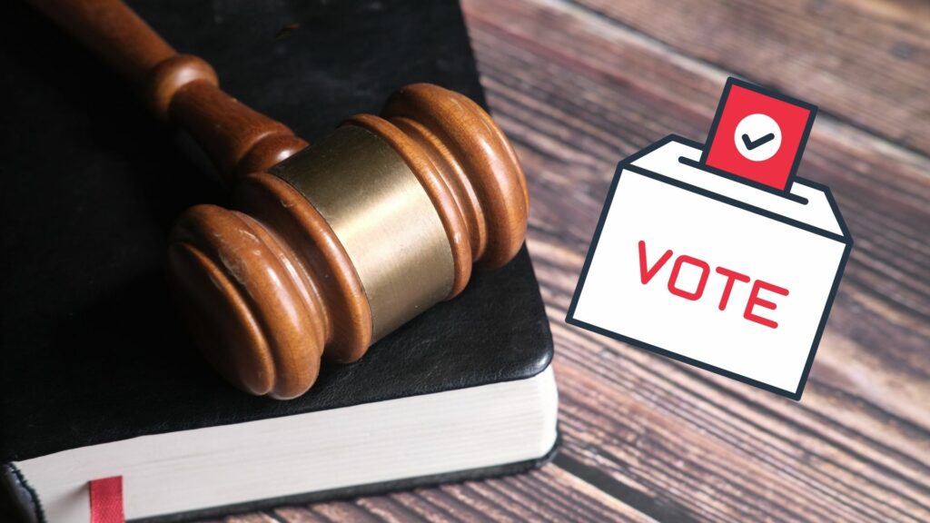 A gavel sitting on a bible with a cartoon image of a voting ballot box.