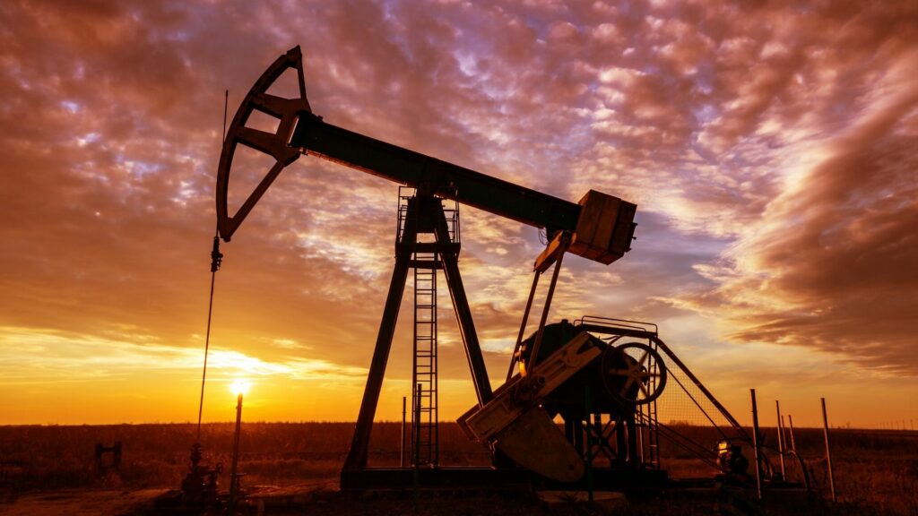 An oil rig silhoutted against a pink and orange sunset.