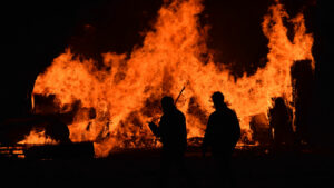 Silhouettes of firefighters against a bright orange flame.