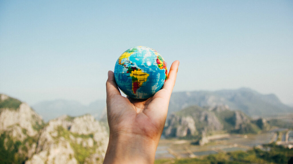 A persons hand holding a small globe outside.