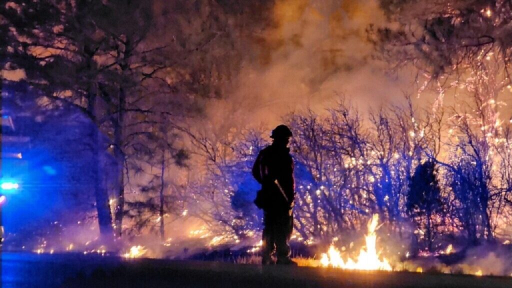A firefighter silhouetted in front of a wildfire.