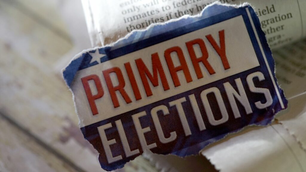 A ripped up piece of paper that says "primary elections" sitting on a newspaper.