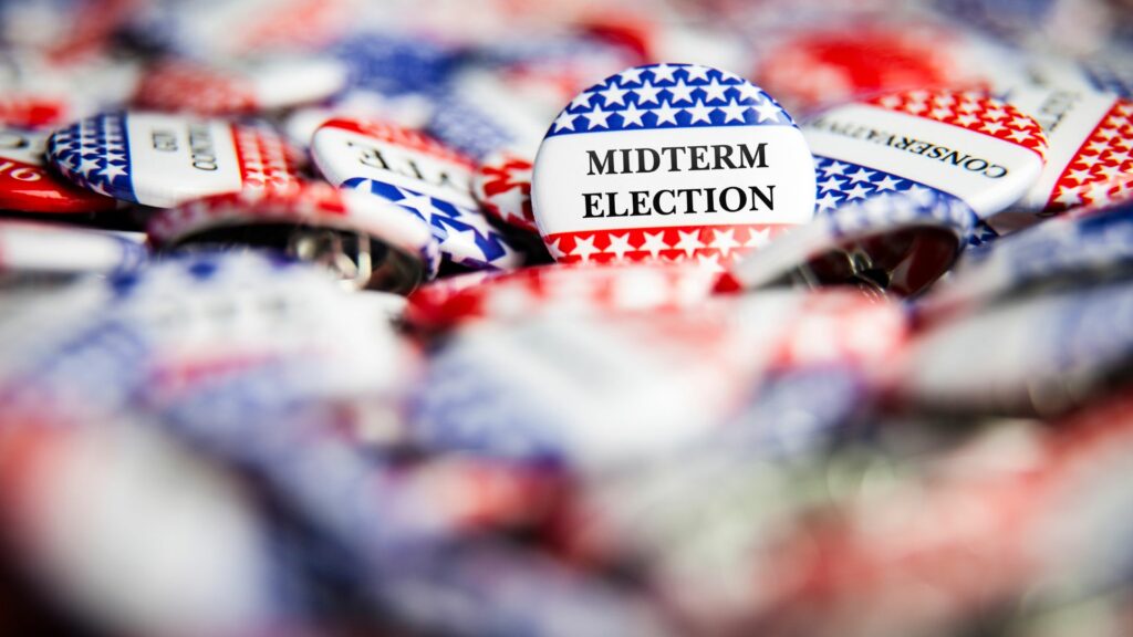 A pile of buttons that say "midterm election" with american flag colors and designs.