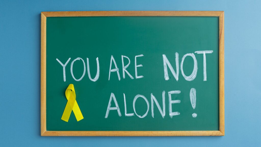 A chalk board with the message "you are not alone!" written on it with a yellow ribbon pinned to it.
