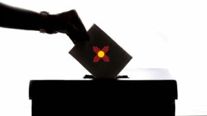 A silhouette of a person voting and putting their ballot in a box.