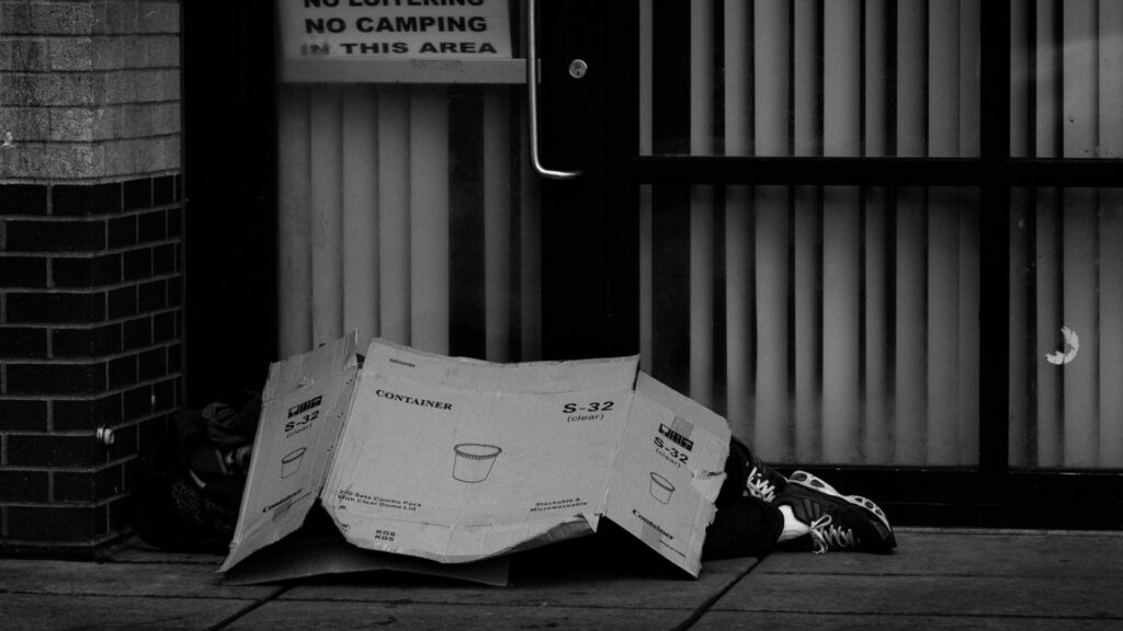 Homeless person sleeping on the sidewalk with a flat cardboard box as a blanket.