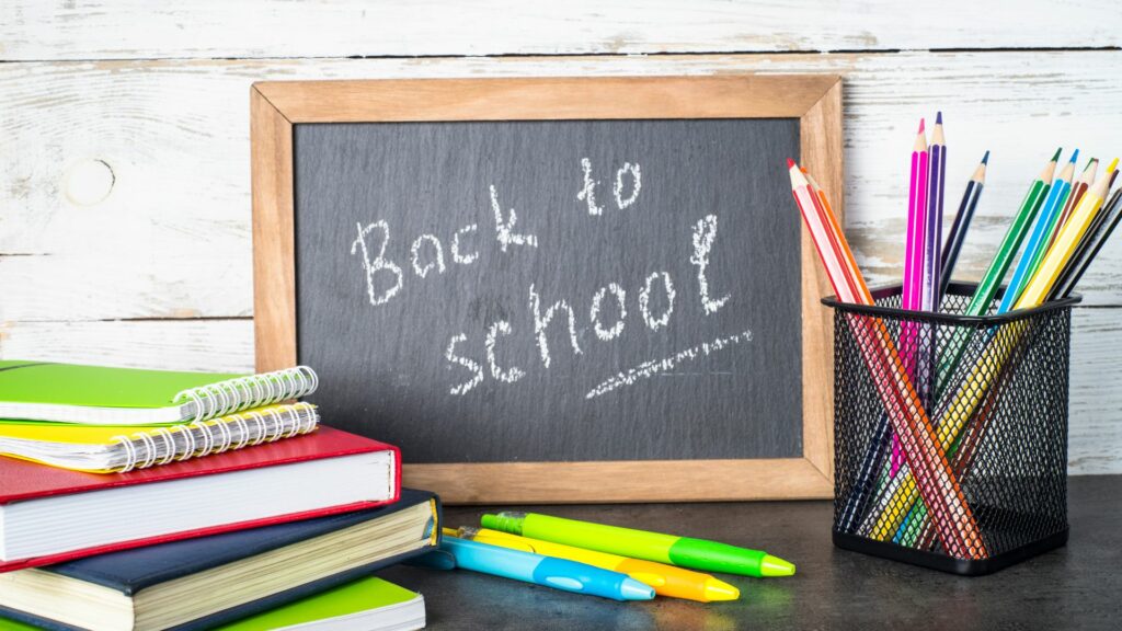 A chalkboard with "Back to School" written in chalk with school supplies scattered around it.