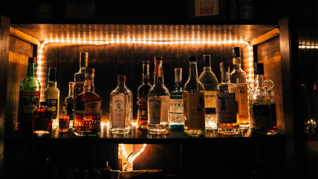 Many bottles of liquor are lined up on a shelf.