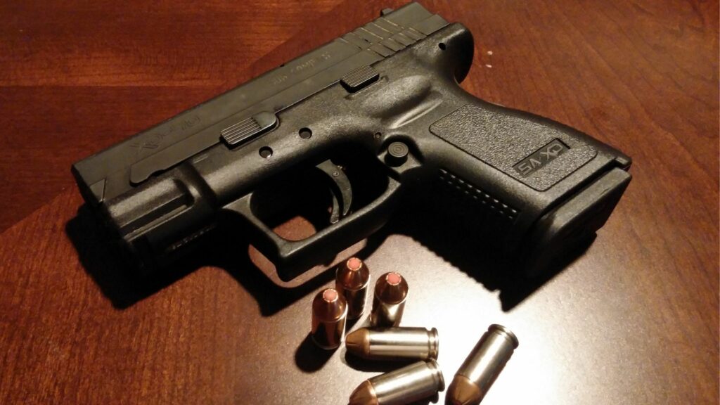 A gun with bullets laying on a wooden table.