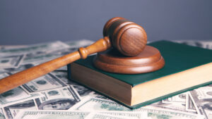 A gavel resting on a green book laying on top of a pile of money.