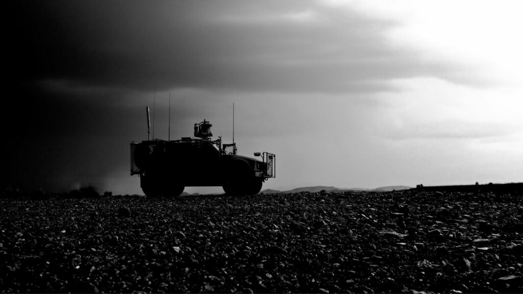 A black and white silhouette of an military vehicle going down a dirt road.