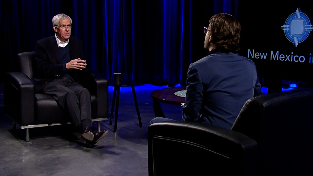 Two men sitting in chairs in front of a blue screen.