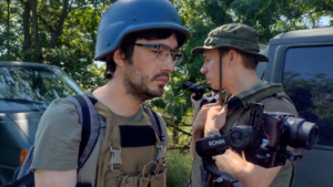 A man in a helmet is talking to a man in a camcorder.