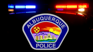 A picture of a police vehicle with it's lights on in the dark with the Albuquerque Police Logo superimposed.