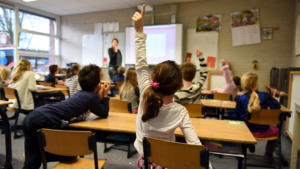 A classroom full of children raising their hands.