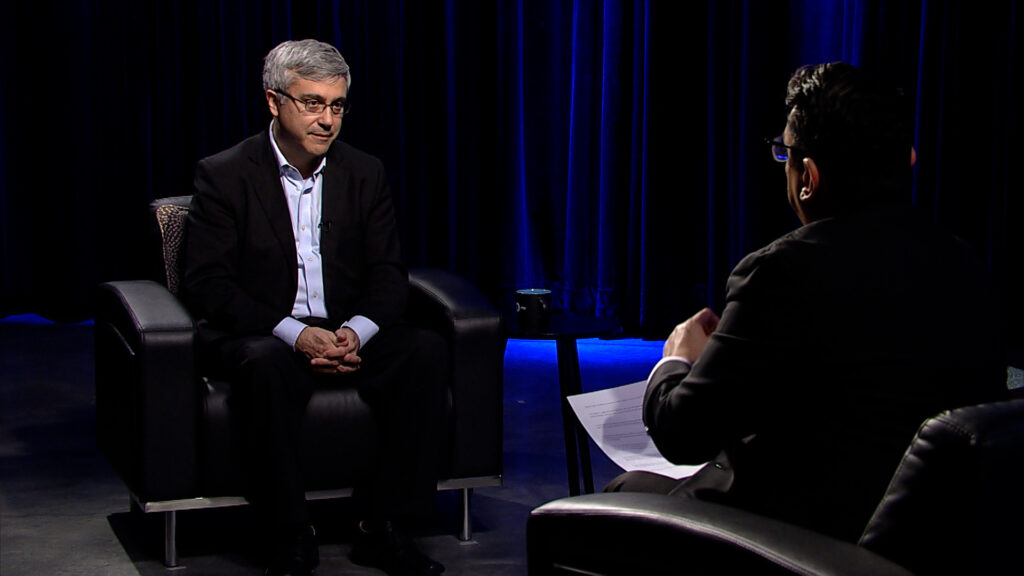 A man sitting in a chair talking to another man.