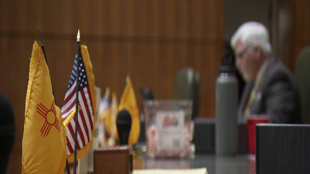 A man sits at a table with flags in front of him.