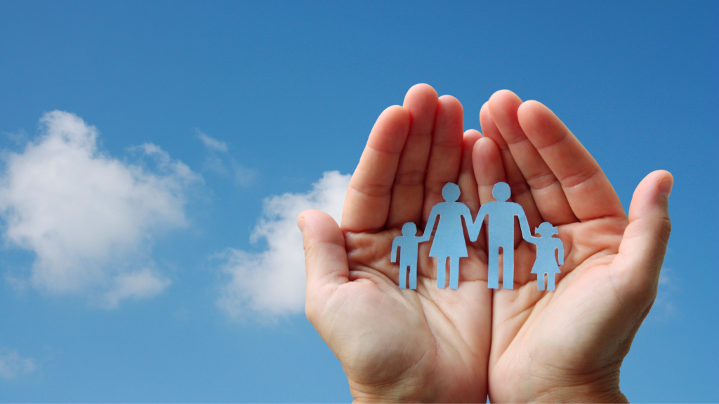 A person holding a paper cut out of a family with the sky behind their hands.