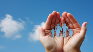 A person holding a paper cut out of a family with the sky behind their hands.