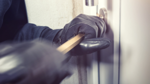 A person trying to break into a door with a crow bar wearing black gloves.