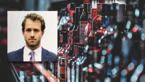 A man in a suit is standing in front of a bar full of bottles.