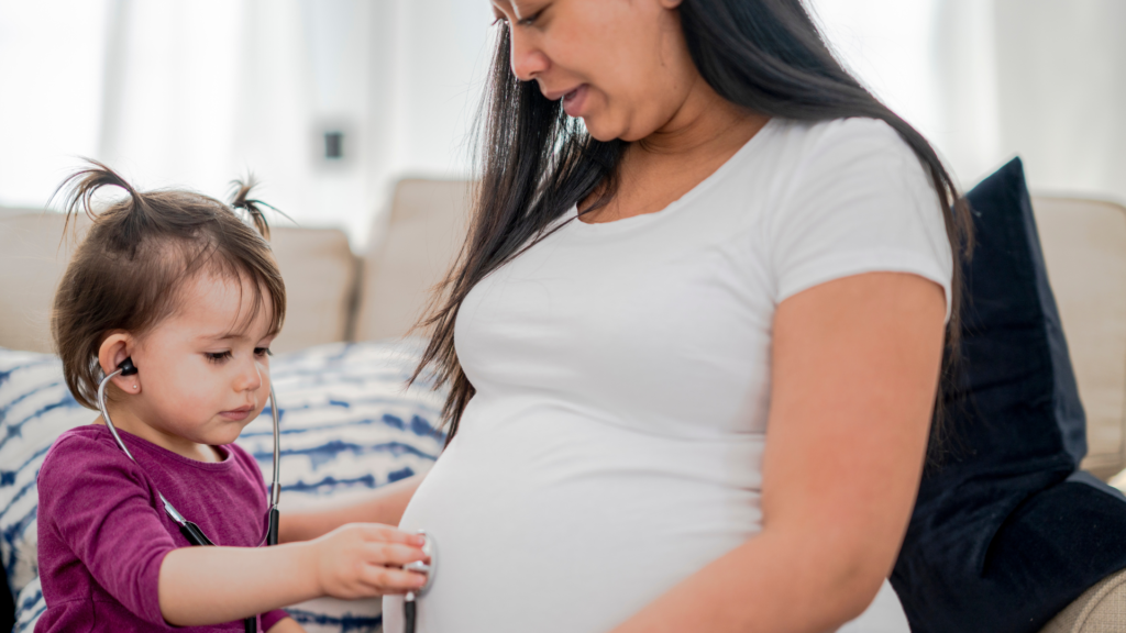 A pregnant woman with a little girl looking at an earphone.