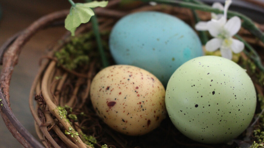 Three colorful easter eggs in a basket on a table.
