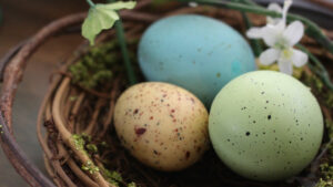 Three colorful easter eggs in a basket on a table.