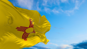 The New Mexico state flag flapping in the wind with the sky in the background.