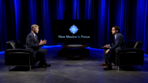 Two men sitting in chairs in front of a blue screen.