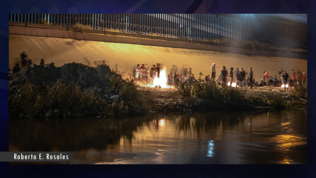 A group of people standing around a campfire near a river.