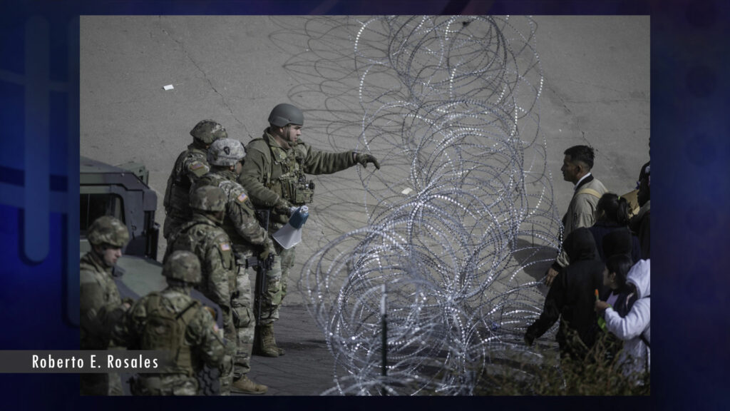 A group of soldiers standing next to a barbed wire fence.
