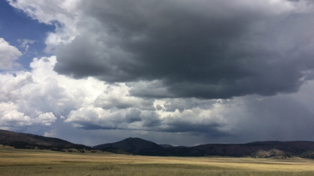 A cloudy sky over a grassy field with mountains in the background.