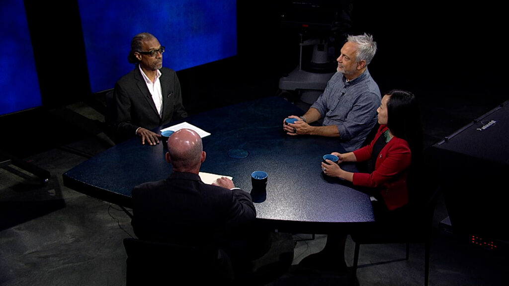 Three people sitting around a table in front of a blue screen.