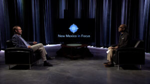 Two men sitting in chairs in front of a screen.