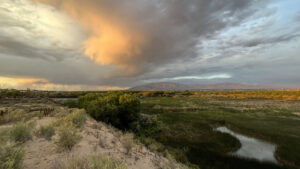 A stormy sky over a grassy area with water in the background.