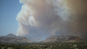 A large cloud of smoke is seen over a mountain range, indicating a potential wildfire.