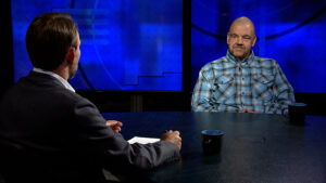 A man sits at a table and talks to a camera.