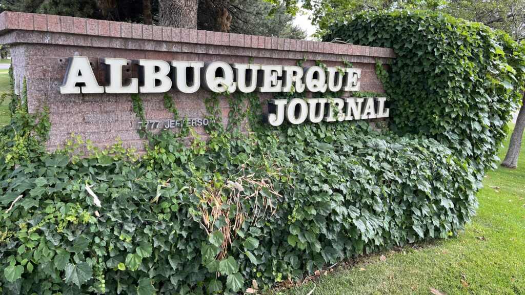 Albuquerque journal sign in front of bushes.