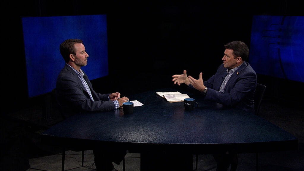 Two men sitting at a table talking to each other.