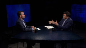 Two men sitting at a table talking to each other.