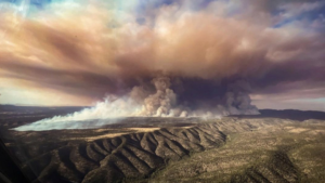 A plane flies over a large fire in california.