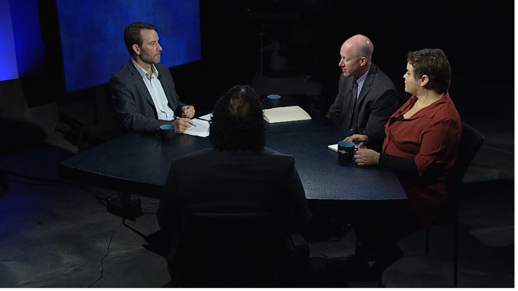 Three people sitting at a table in front of a television screen.