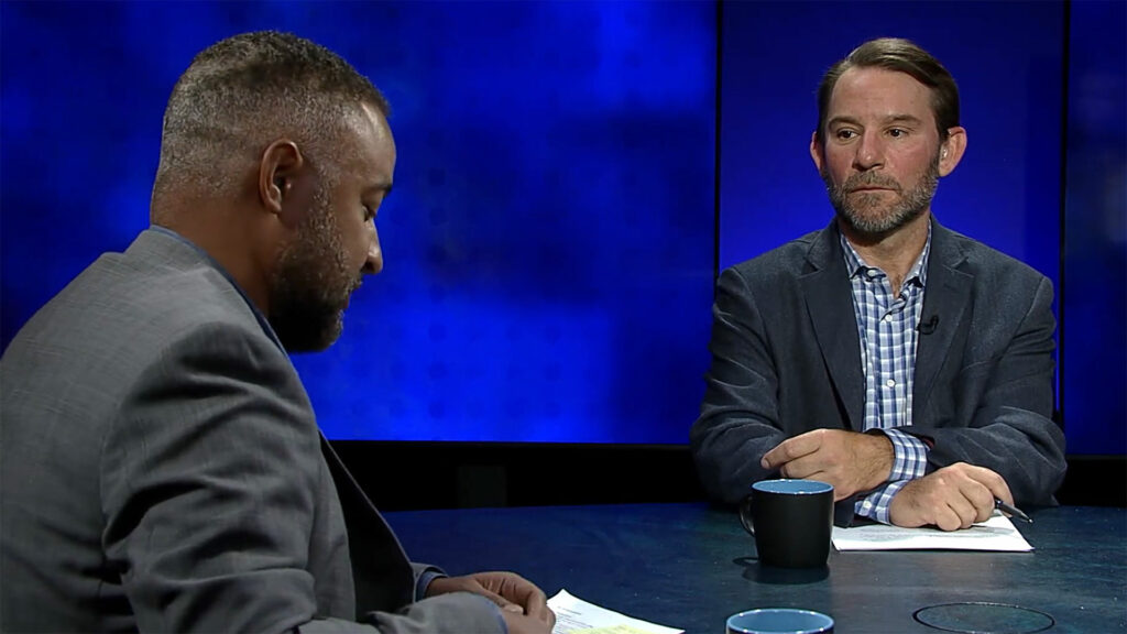 Two men sitting at a table talking to each other.